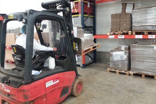 Operario en empresa logística efectuando su trabajo cargando mercancía y transportandola a otra parte del almacén.